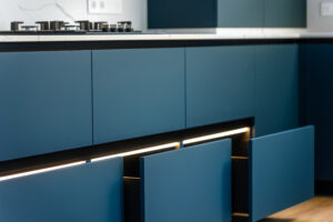 Matte blue base cabinets with a continuous LED strip under the countertop, open drawers guide the eye toward the gas cook top.
