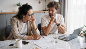 Couple sitting at a white table with a laptop going over paperwork